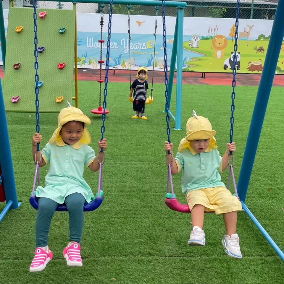 Two children in sun hats on swings in the school playground