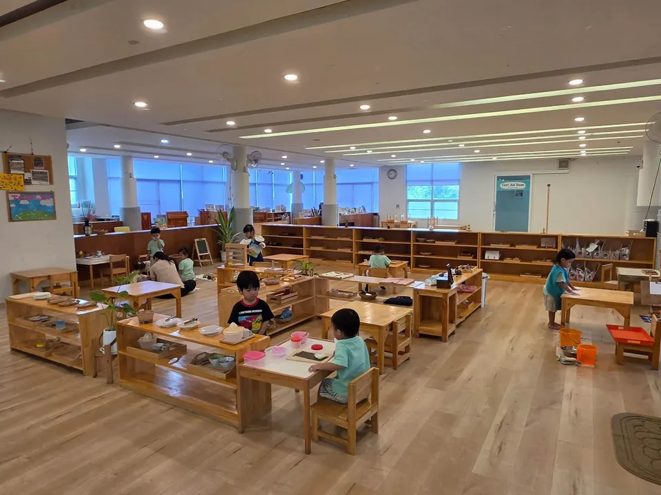 A wide, bright Montessori classroom with wooden shelves and children working at small tables