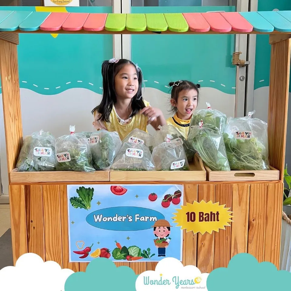 Two girls behind a wooden market stall with bags of vegetables